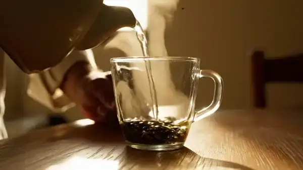 Loose green tea leaves slowly unfurling in a clear glass cup of hot water