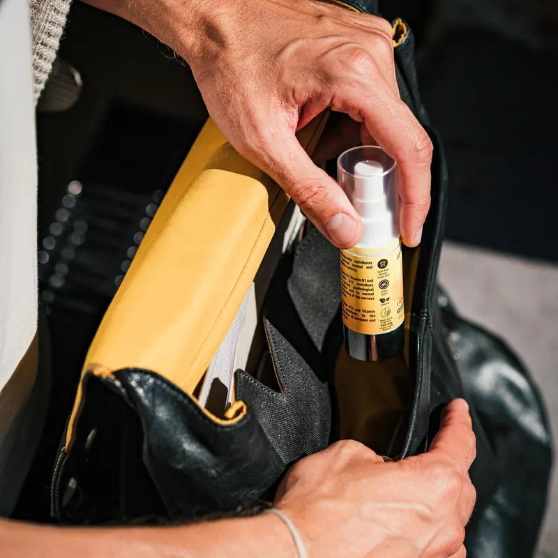 A hand taking the small Shroomwell spray bottle out of a leather bag, from the seller's own photograph